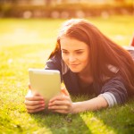 Beautiful girl with tablet or ebook outdoor laying on field
